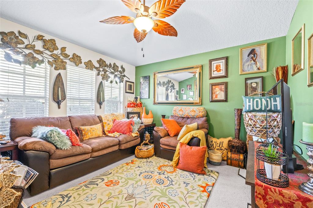 A living room features a brown sofa, an armchair, a green wall, and a ceiling fan — 7113 CROMWELL PARK LANE, APOLLO BEACH, FL