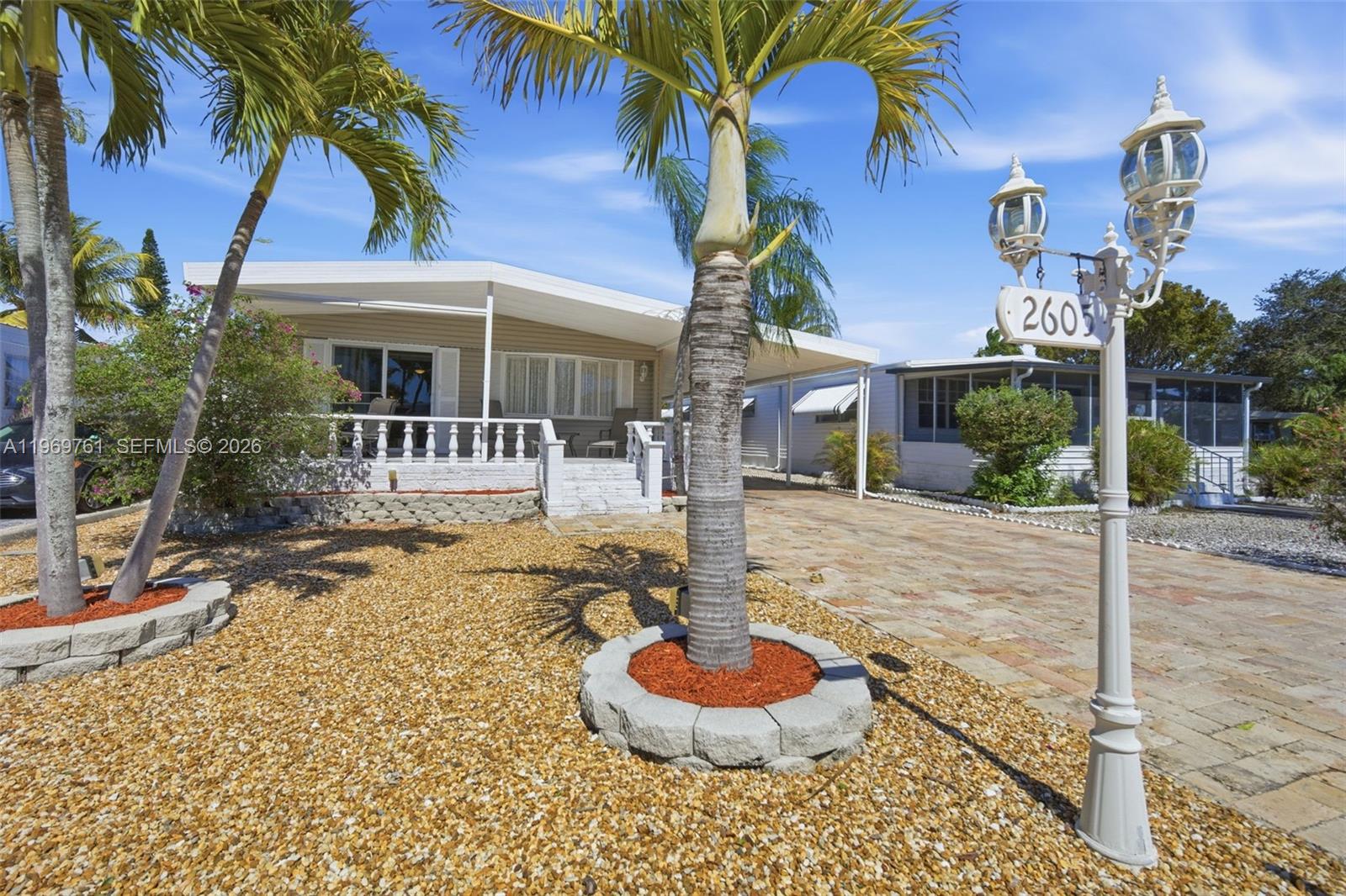 A single-story mobile home features a front porch, a paved driveway, and palm trees — 2605 E Marina Dr, Dania Beach FL 33312, DANIA BEACH, FL