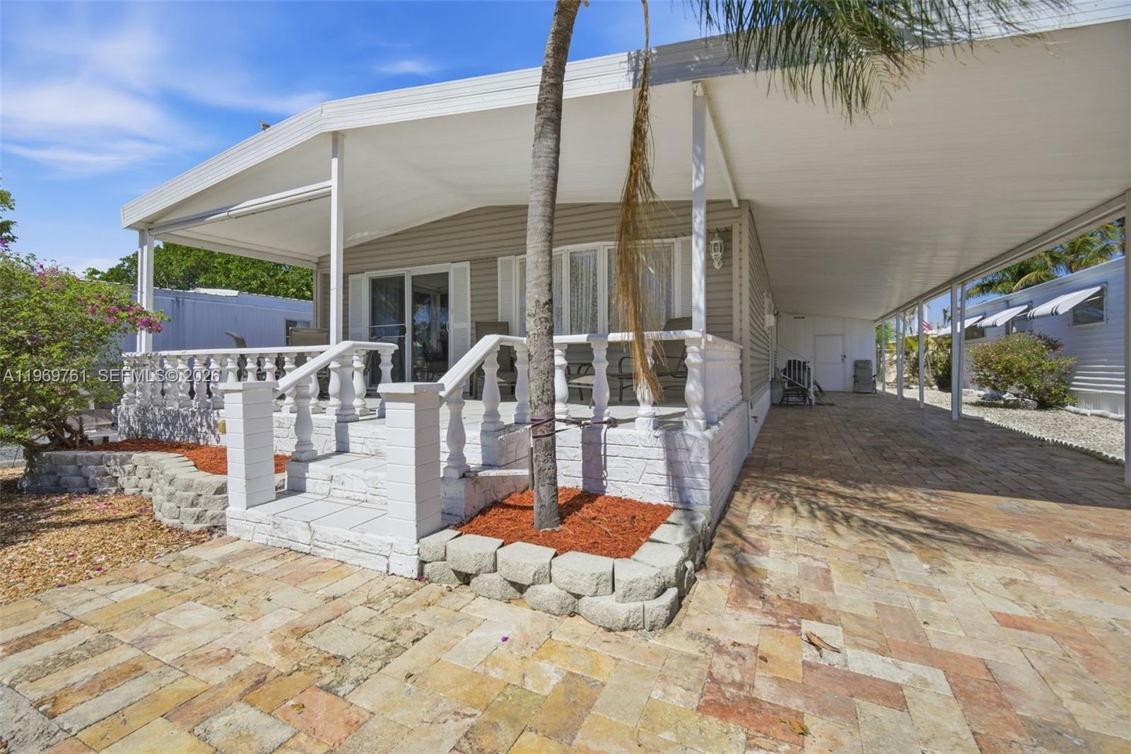 A manufactured home features a paved driveway, a covered porch with white railings, and landscaping — 2605 E Marina Dr, Dania Beach FL 33312, DANIA BEACH, FL