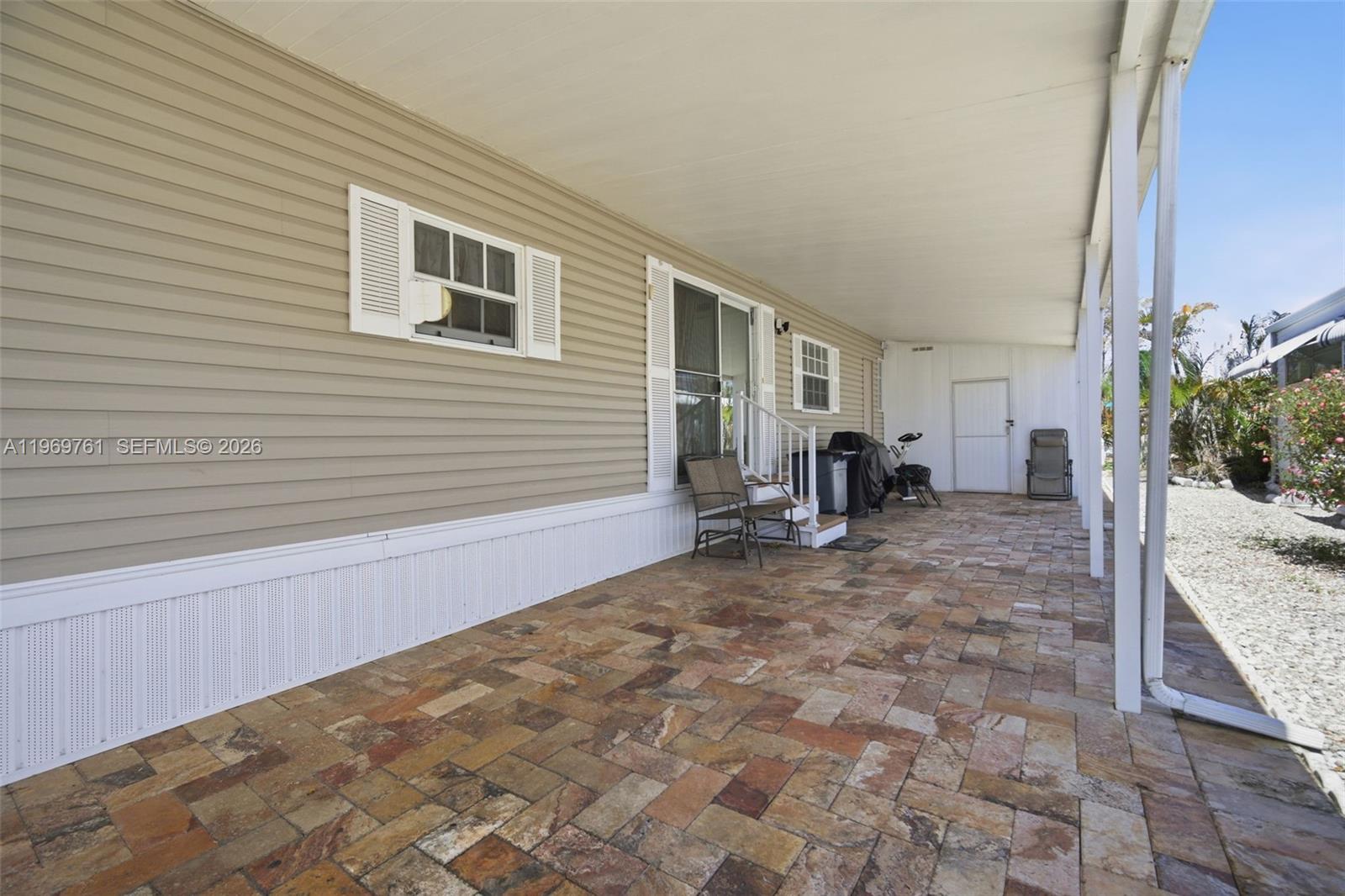 A covered patio with stone pavers sits beside the beige vinyl siding of a home — 2605 E Marina Dr, Dania Beach FL 33312, DANIA BEACH, FL