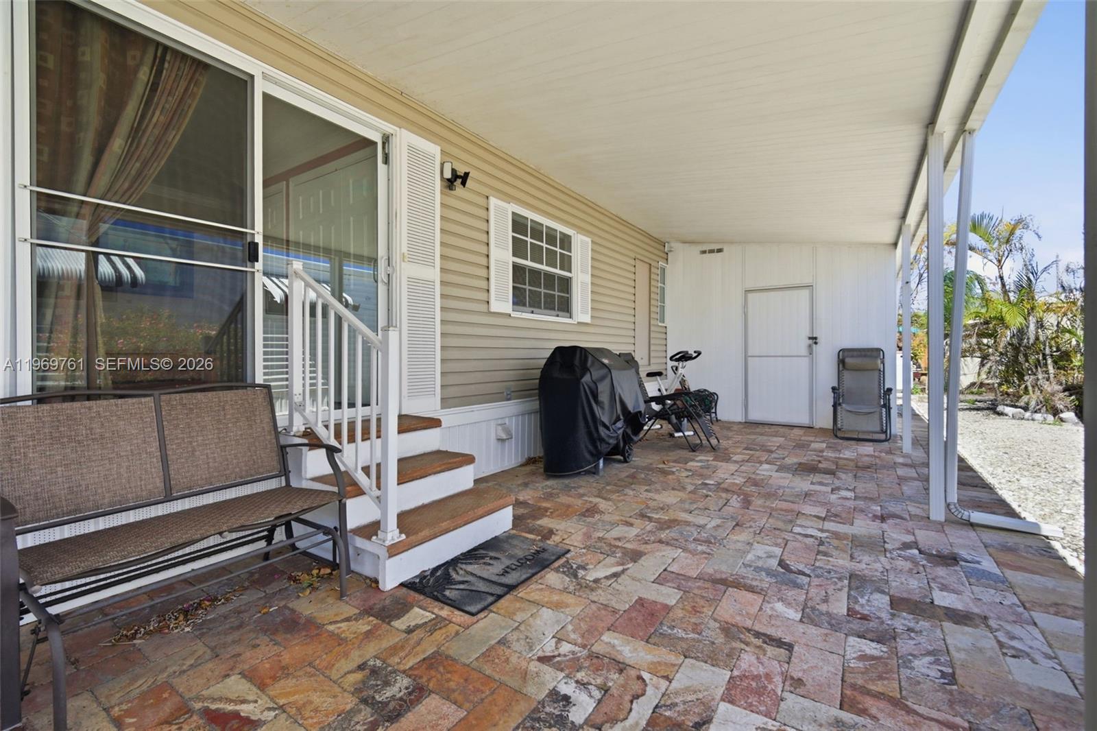 A covered patio features stone-look pavers, a grill, exercise equipment, and steps to a sliding door — 2605 E Marina Dr, Dania Beach FL 33312, DANIA BEACH, FL