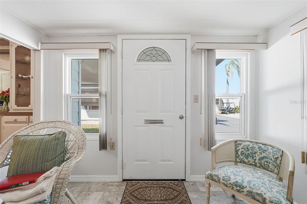 A sunroom with a white front door, two windows, tiled floors, and two wicker chairs — 82209 F STREET N UNIT 209, PINELLAS PARK, FL