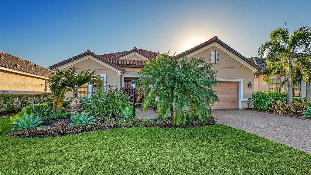 A single-story house with a tan stucco exterior, tile roof, and a landscaped front yard — 15410 DERNA TERRACE, LAKEWOOD RANCH, FL
