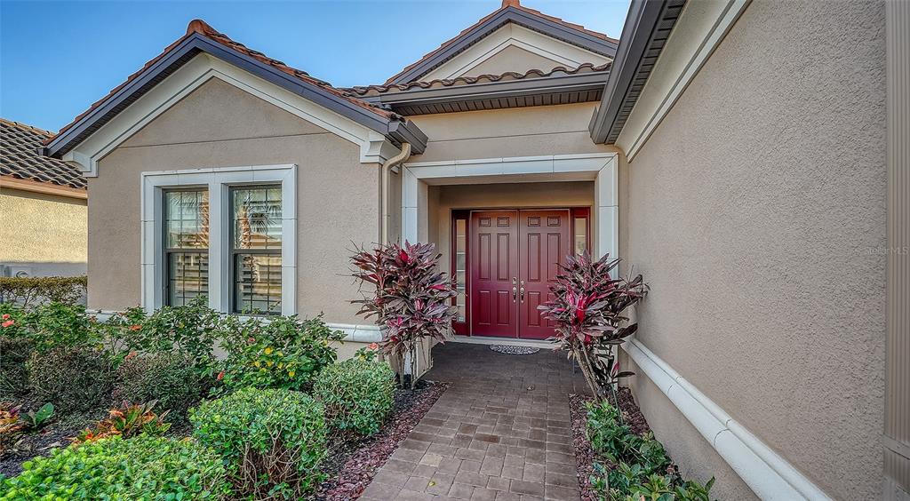 The exterior of a house features a paved walkway leading to a double red front door — 15410 DERNA TERRACE, LAKEWOOD RANCH, FL