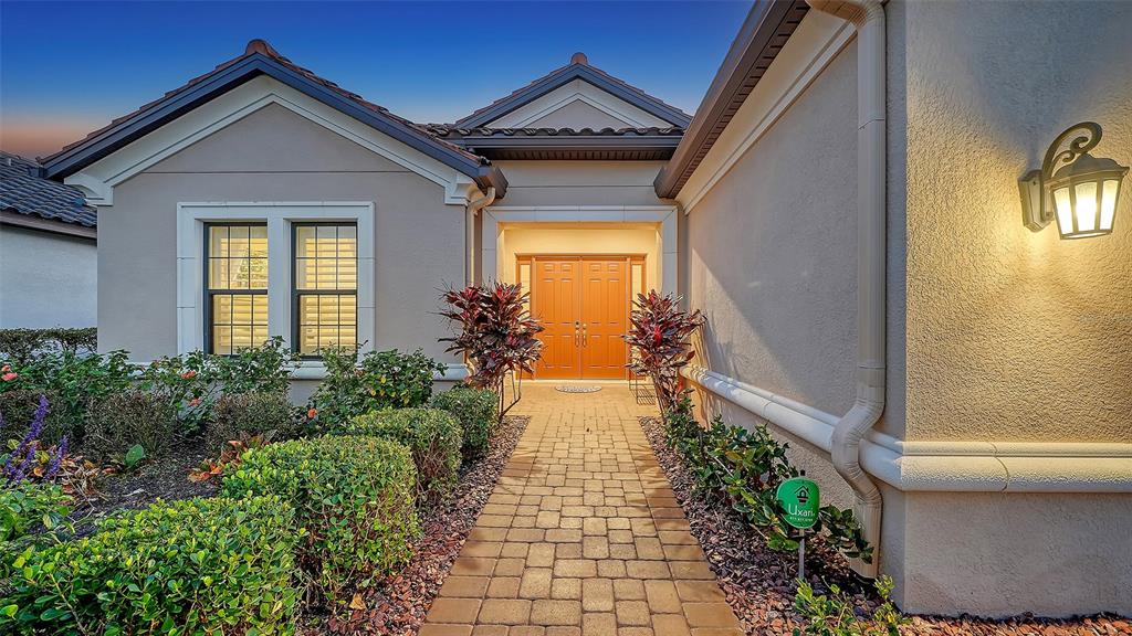 A paved walkway leads to the double front doors of a beige stucco house — 15410 DERNA TERRACE, LAKEWOOD RANCH, FL