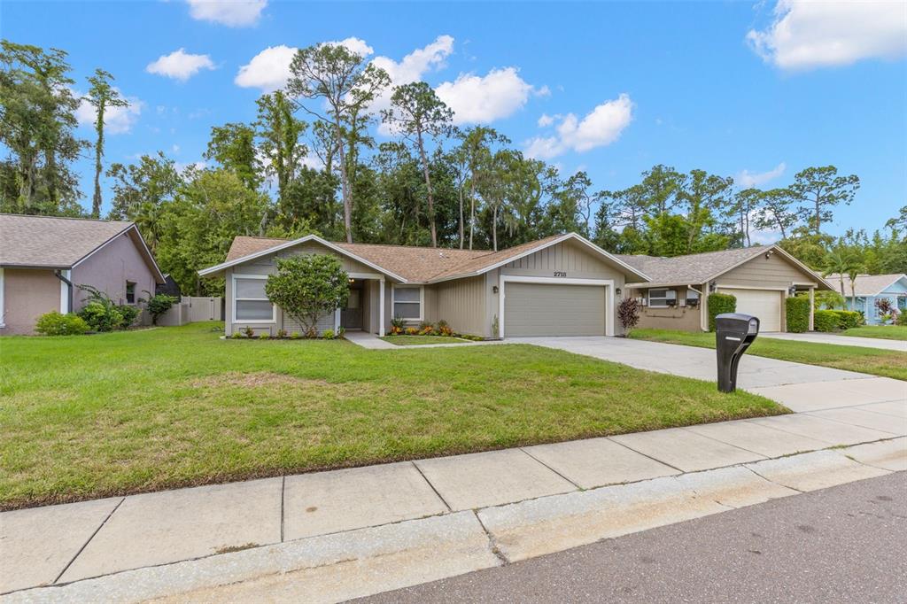 A single-story house with a tan exterior, a two-car garage, and a front lawn — 2718 WOODHALL TERRACE, PALM HARBOR, FL