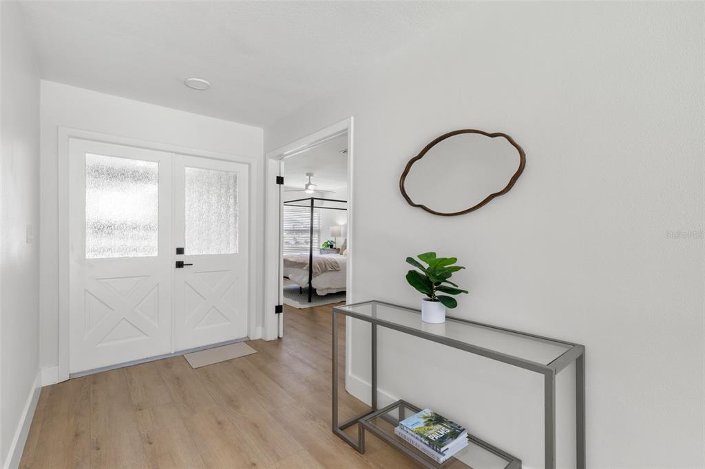 A bright entryway features a white double door, light wood flooring, and a glass console table — 2718 WOODHALL TERRACE, PALM HARBOR, FL