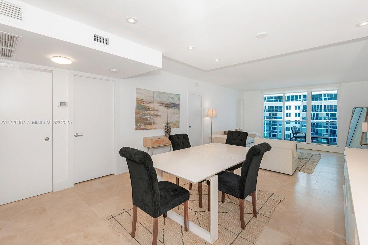 A dining area with a white table and black chairs sits before a living space — 2301 Collins Ave # 1515, Miami Beach FL 33139, MIAMI BEACH, FL