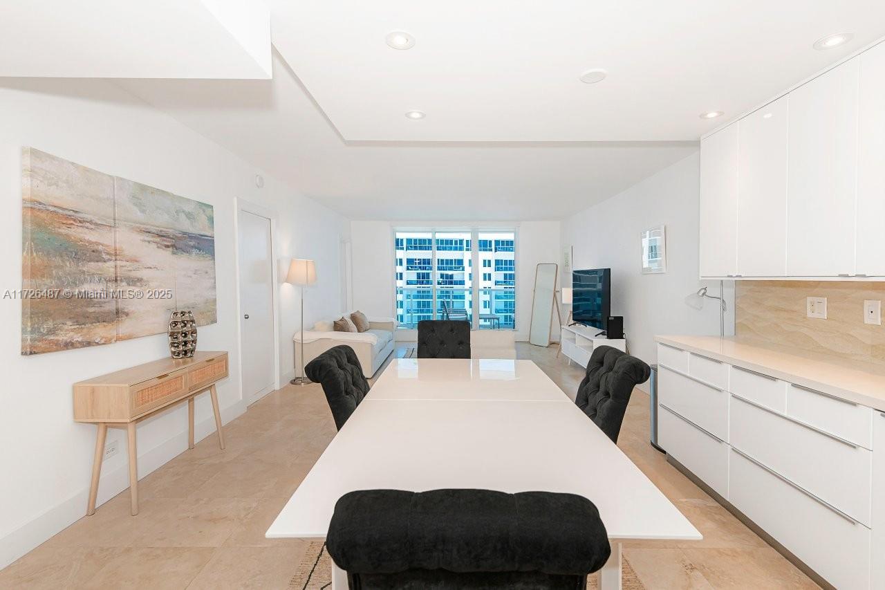A modern dining area features a white table, black tufted chairs, and white cabinetry — 2301 Collins Ave # 1515, Miami Beach FL 33139, MIAMI BEACH, FL