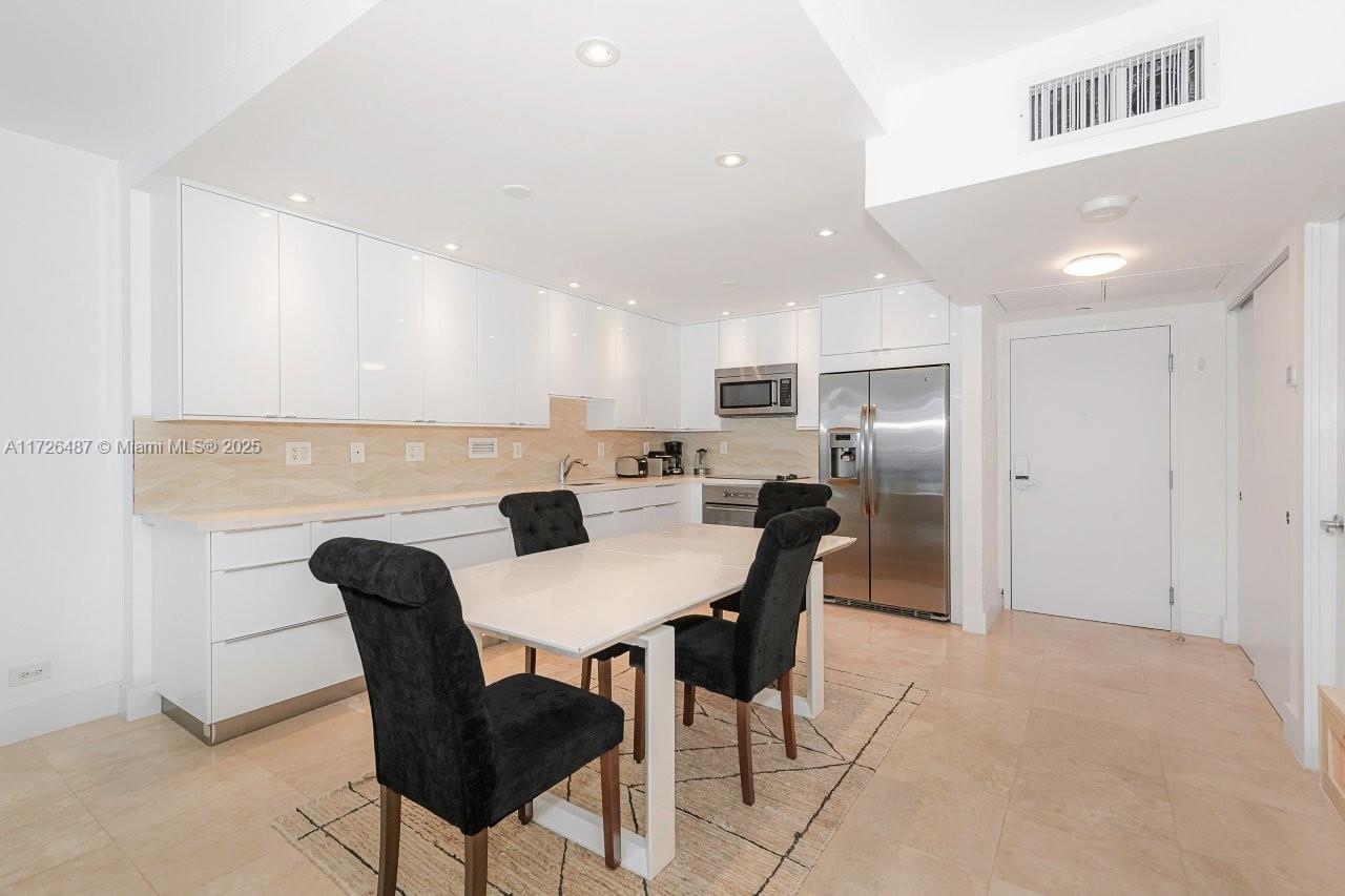 A modern kitchen features white cabinetry, stainless steel appliances, and a dining table with chairs — 2301 Collins Ave # 1515, Miami Beach FL 33139, MIAMI BEACH, FL
