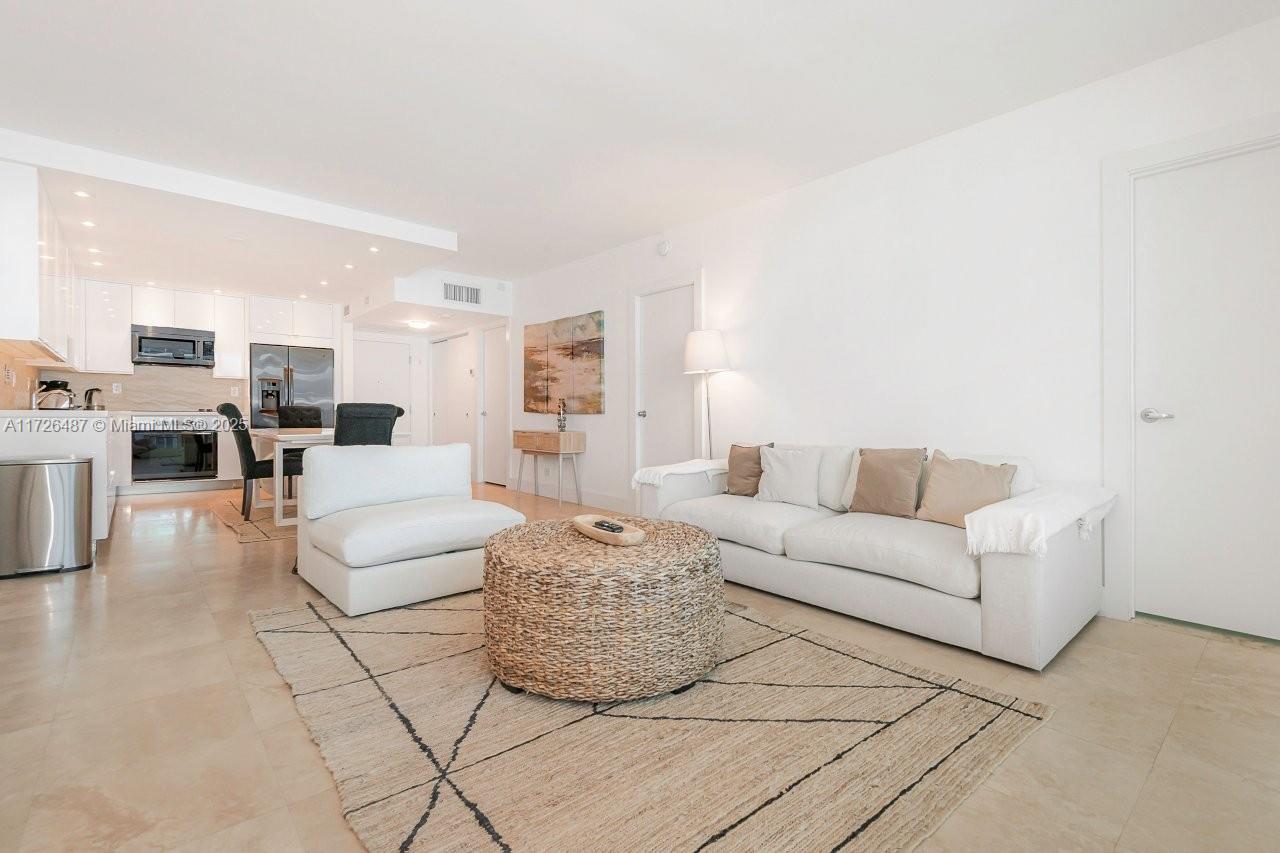 A bright living room features a white sofa, a woven ottoman, and an open kitchen — 2301 Collins Ave # 1515, Miami Beach FL 33139, MIAMI BEACH, FL