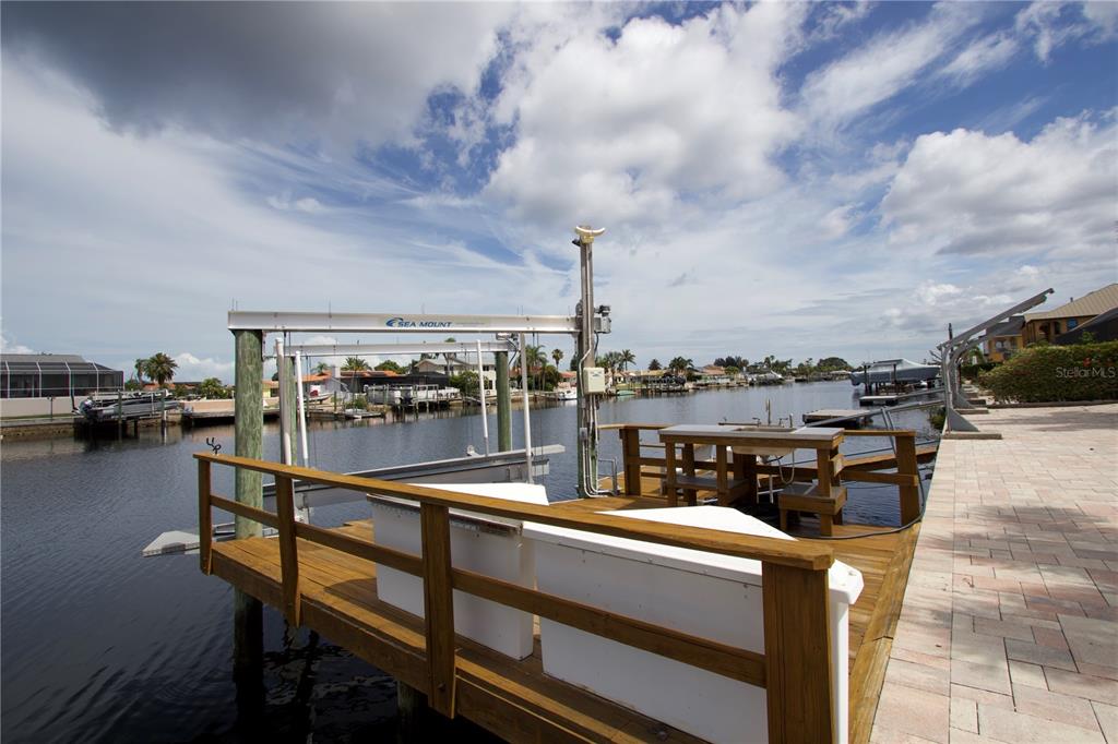 A wooden dock features a boat lift and a small table overlooking a canal — 5339 BOWLINE BEND, NEW PORT RICHEY, FL