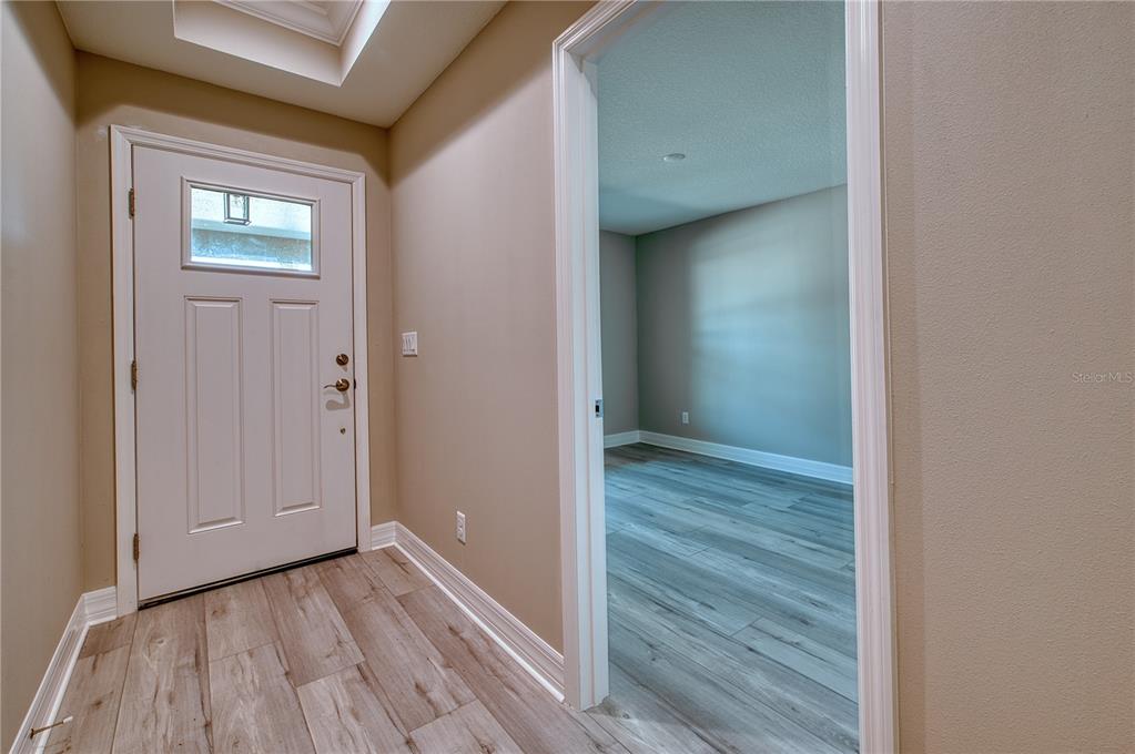 An entryway with light wood-look flooring leads into a room through an open doorway — 1183 CEDAR AVENUE, ENGLEWOOD, FL