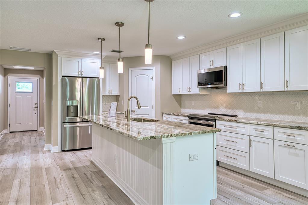 A modern kitchen features white cabinetry, a granite-topped island, stainless steel appliances, and wood flooring — 1183 CEDAR AVENUE, ENGLEWOOD, FL
