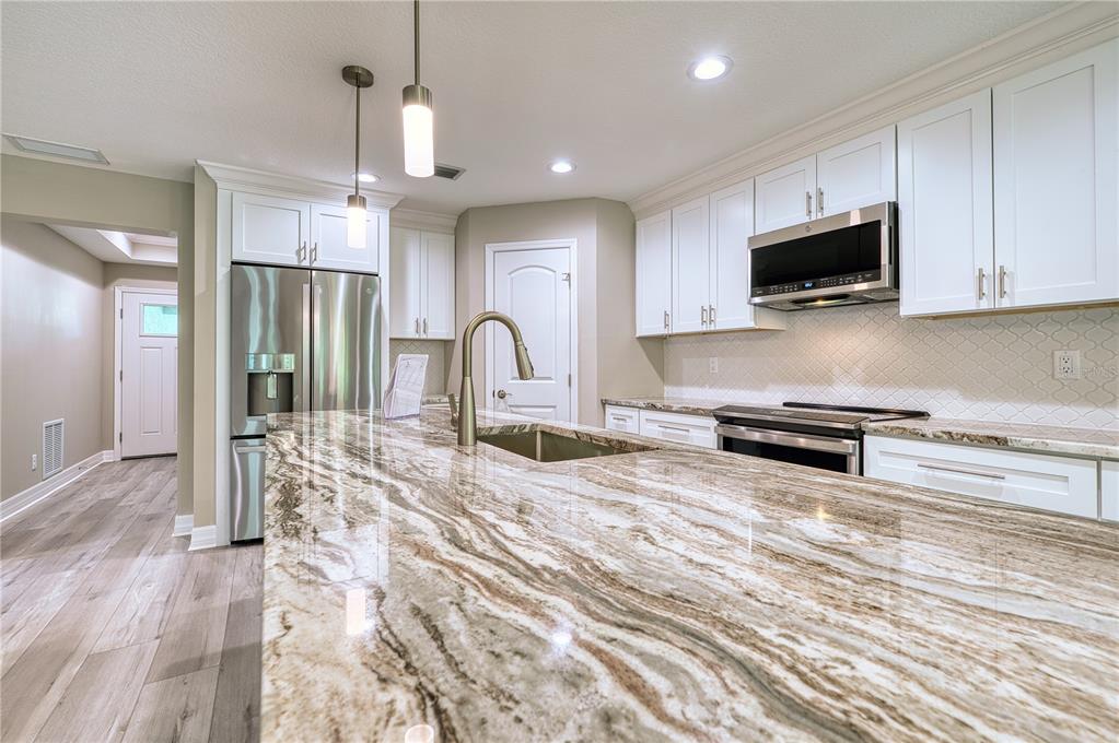 A kitchen features white cabinets, stainless steel appliances, and a large granite-topped island — 1183 CEDAR AVENUE, ENGLEWOOD, FL