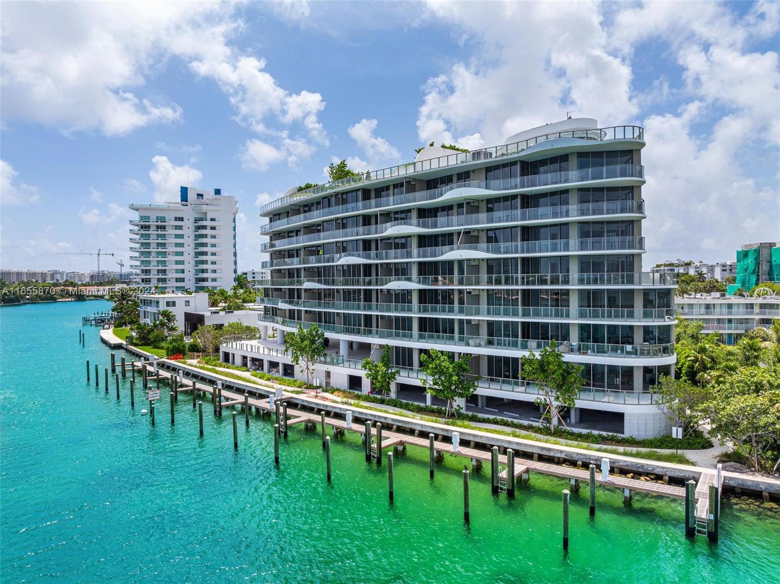 An aerial view of a modern, multi-story residential building situated along a turquoise waterfront — 1135 103 St # 202, Bay Harbor Islands FL 33154, BAY HARBOR ISLANDS, FL