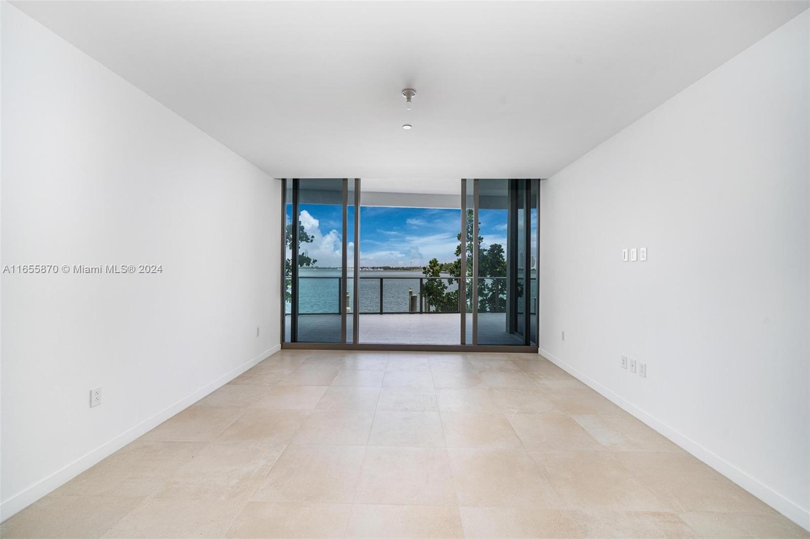 An empty room with light tile flooring features large sliding glass doors opening to a balcony — 1135 103 St # 202, Bay Harbor Islands FL 33154, BAY HARBOR ISLANDS, FL