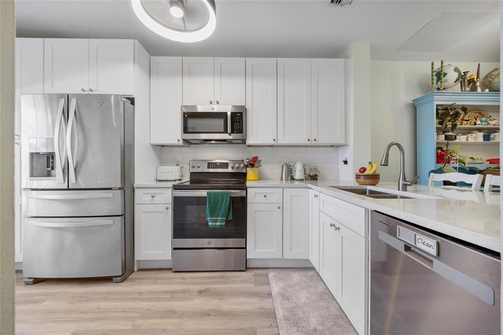 A kitchen features white cabinets, stainless steel appliances, and light wood-look flooring — 5937 BAYSIDE KEY DRIVE, TAMPA, FL