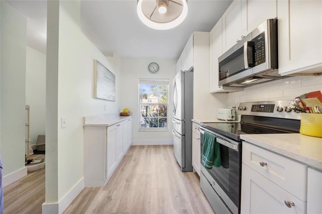 A galley kitchen features white cabinets, stainless steel appliances, light wood flooring, and a window — 5937 BAYSIDE KEY DRIVE, TAMPA, FL