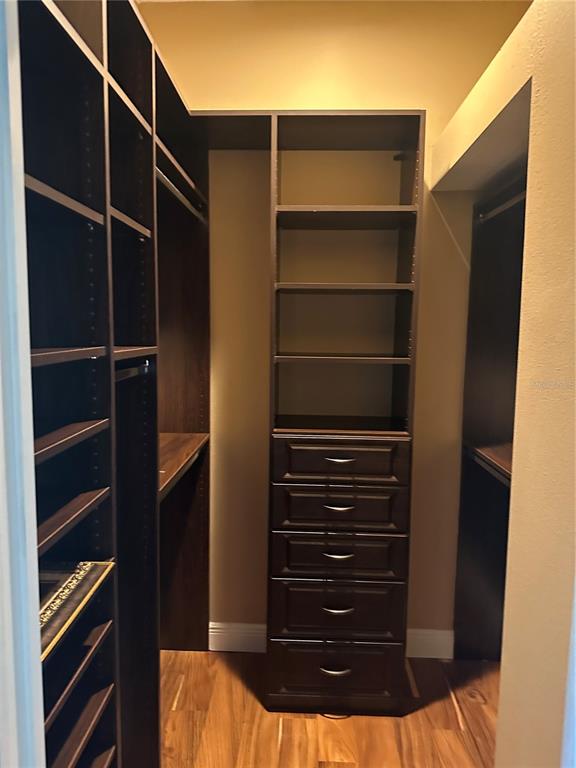 A walk-in closet features dark wood shelving, a built-in dresser, and light wood flooring — 7135 KENSINGTON COURT, UNIVERSITY PARK, FL