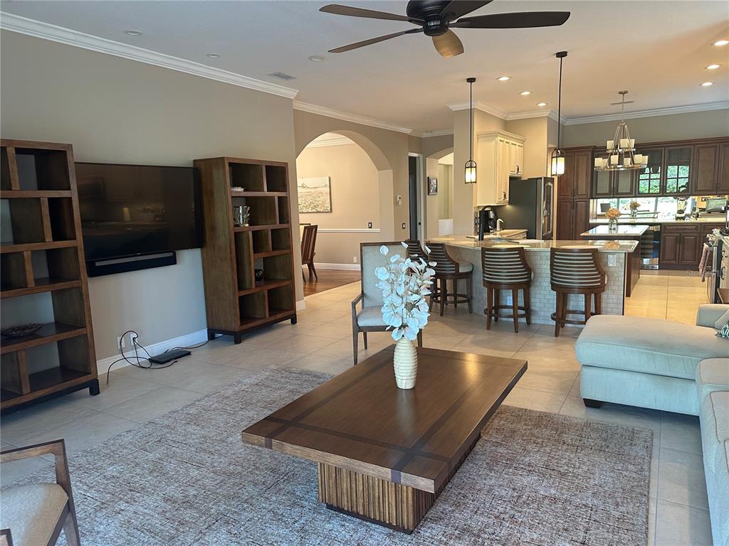A living room with a coffee table, bookshelves, and an open kitchen with bar seating — 7135 KENSINGTON COURT, UNIVERSITY PARK, FL