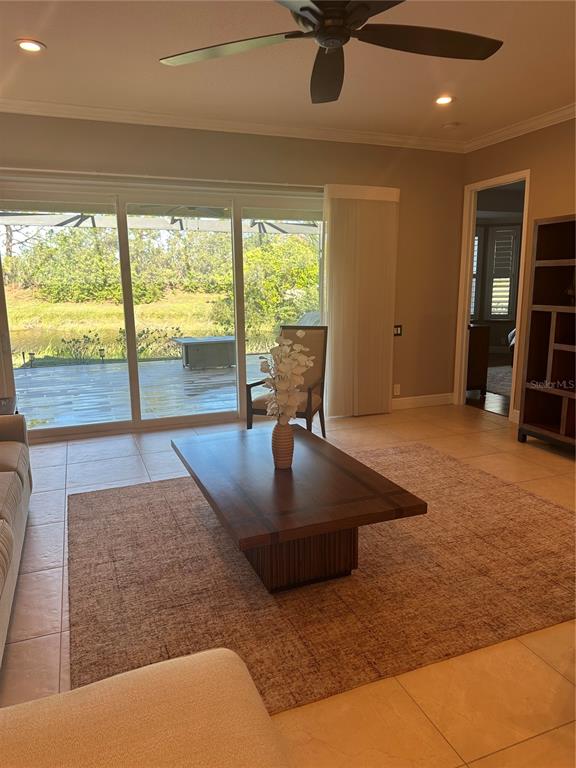 A living room features a wooden coffee table, tile flooring, and sliding doors overlooking a pond — 7135 KENSINGTON COURT, UNIVERSITY PARK, FL