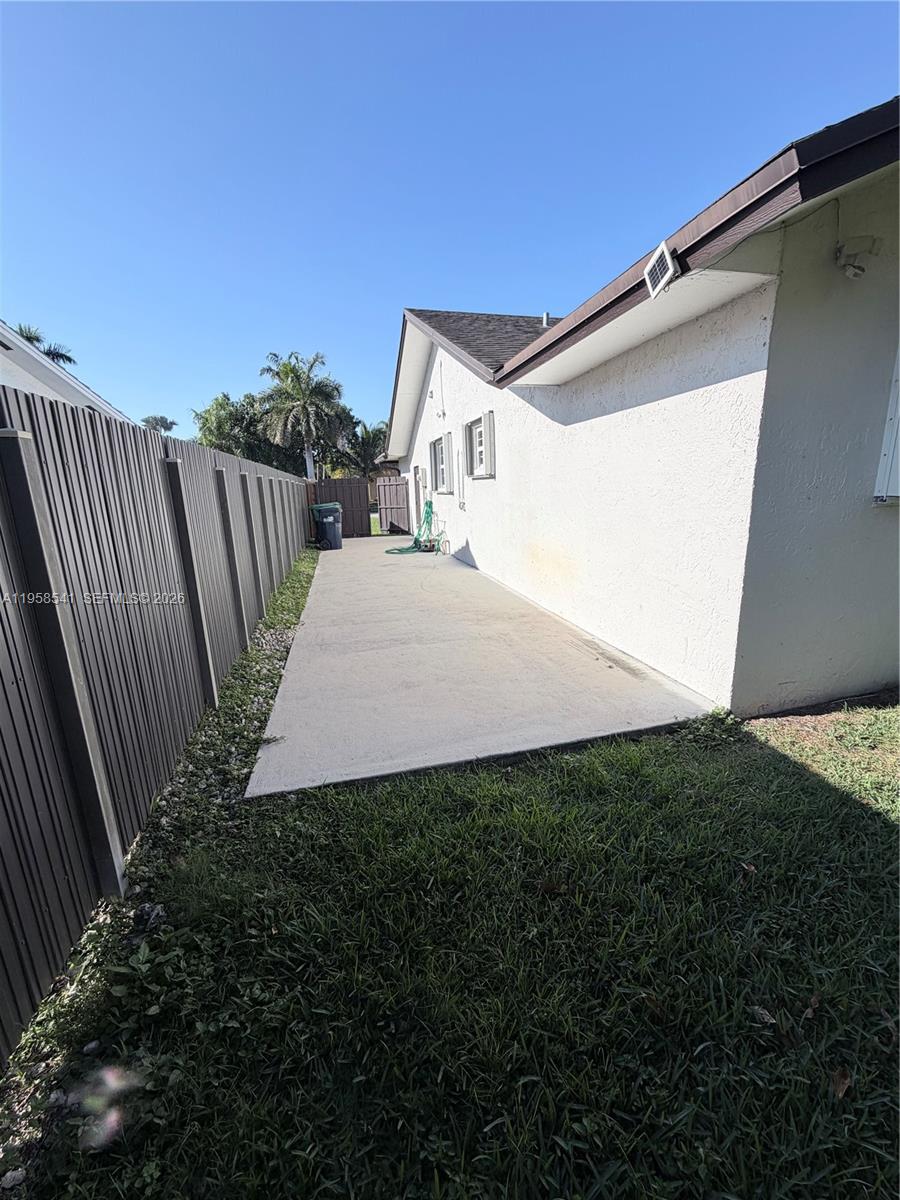 A concrete walkway runs along the side of a house next to a wooden fence — 12821 SW 147th Lane Rd, Miami FL 33186, MIAMI, FL