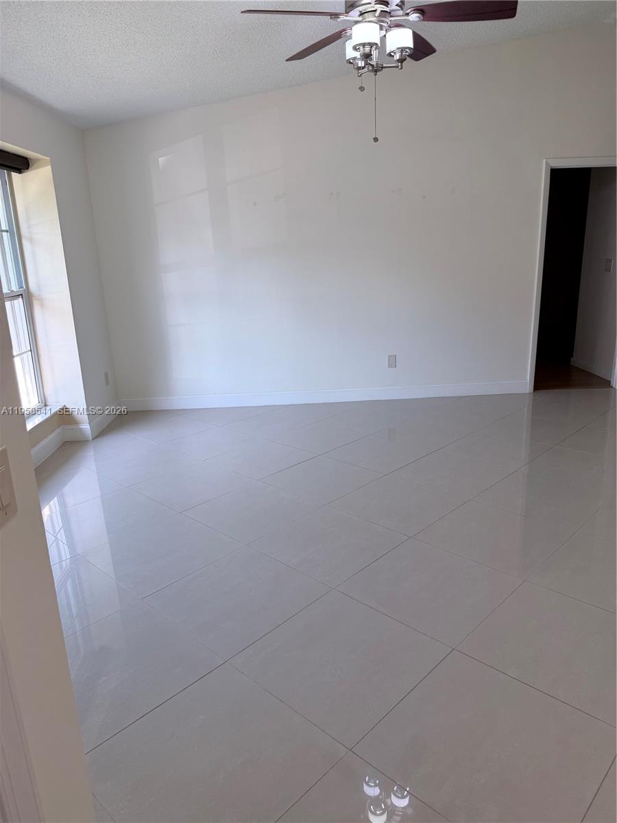 An empty room features white walls, large light-colored floor tiles, and a ceiling fan — 12821 SW 147th Lane Rd, Miami FL 33186, MIAMI, FL