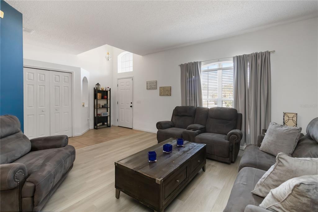 A living room features light wood-look flooring, gray furniture, and a high vaulted ceiling — 633 LINNET COURT, KISSIMMEE, FL