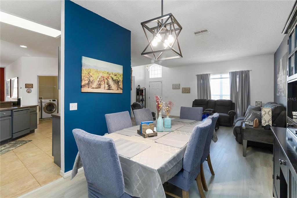 A dining area with a blue accent wall, a geometric chandelier, and light wood flooring — 633 LINNET COURT, KISSIMMEE, FL