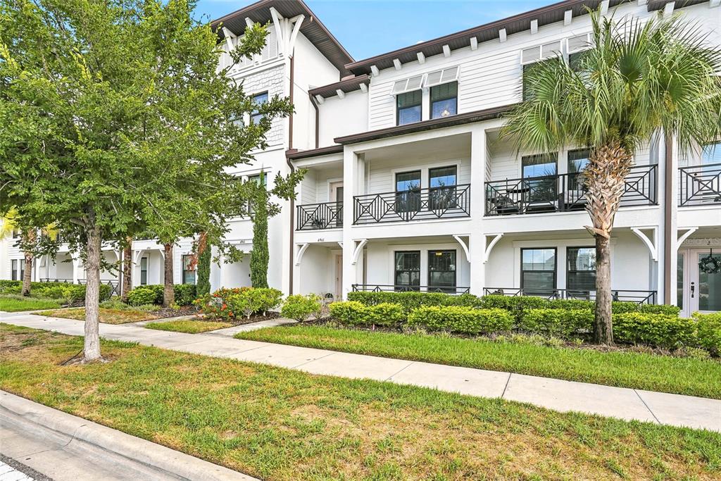 A multi-story white townhouse exterior features balconies, dark-framed windows, and a landscaped front yard — 4941 W PRICE AVENUE UNIT 3, TAMPA, FL