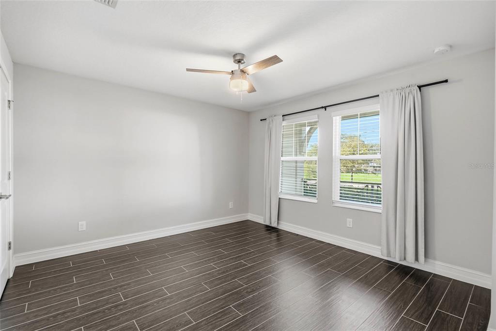 An empty bedroom features light gray walls, dark wood-look tile flooring, and two windows — 4941 W PRICE AVENUE UNIT 3, TAMPA, FL