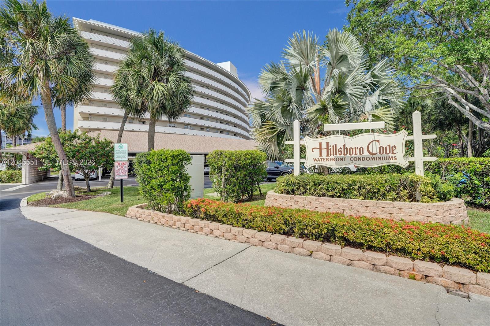 A sign for Hillsboro Cove Waterfront Condominiums stands in front of a curved apartment building — 1301 E Hillsboro Blvd # 307, Deerfield Beach FL 33441, DEERFIELD BEACH, FL