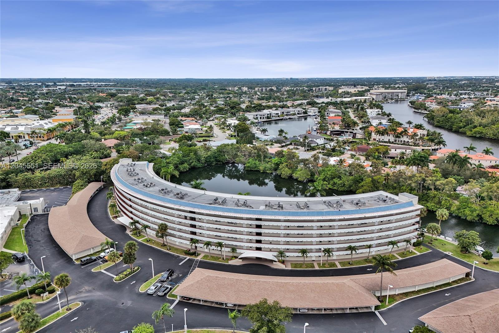 An aerial view shows a curved multi-story residential building situated next to a small lake — 1301 E Hillsboro Blvd # 307, Deerfield Beach FL 33441, DEERFIELD BEACH, FL