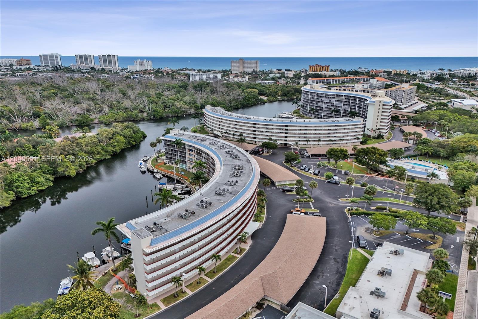 An aerial view shows two curved apartment buildings situated along a waterway near the ocean — 1301 E Hillsboro Blvd # 307, Deerfield Beach FL 33441, DEERFIELD BEACH, FL