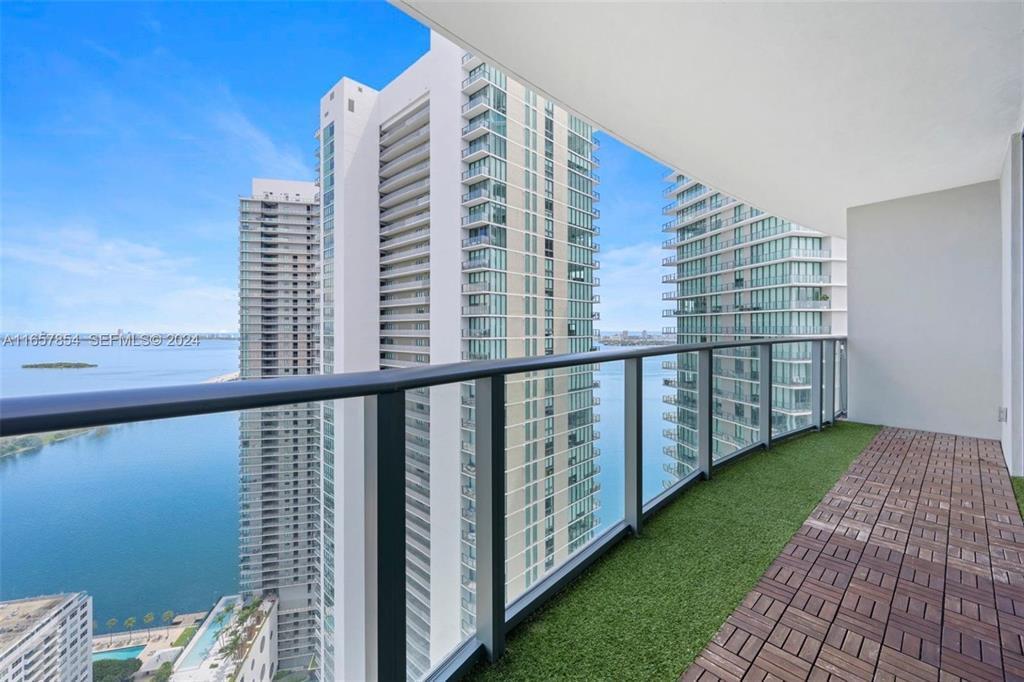 A high-rise balcony features artificial turf, wood deck tiles, and a glass railing overlooking water — 501 NE 31st Street # 3804, Miami FL 33137, MIAMI, FL