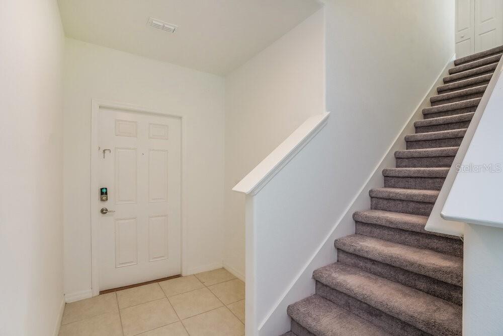 An entryway features a white front door, tiled flooring, and carpeted stairs leading upward — 7308 SPRING SNOWFLAKE AVENUE, TAMPA, FL