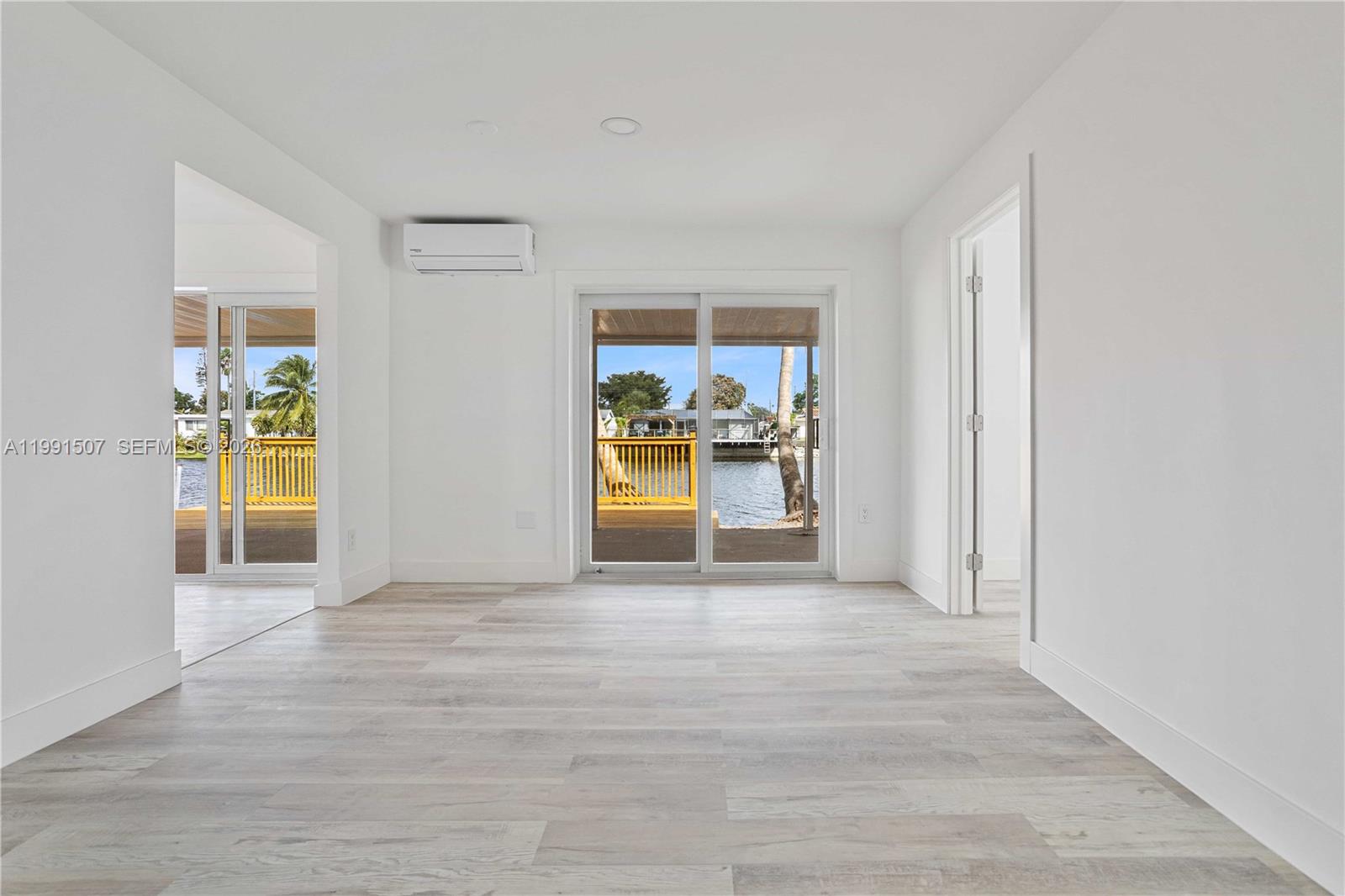 A bright room with light wood-look flooring, a mini-split unit, and sliding doors to water — 4157 SW 49th Ct, Dania Beach FL 33314, DANIA BEACH, FL