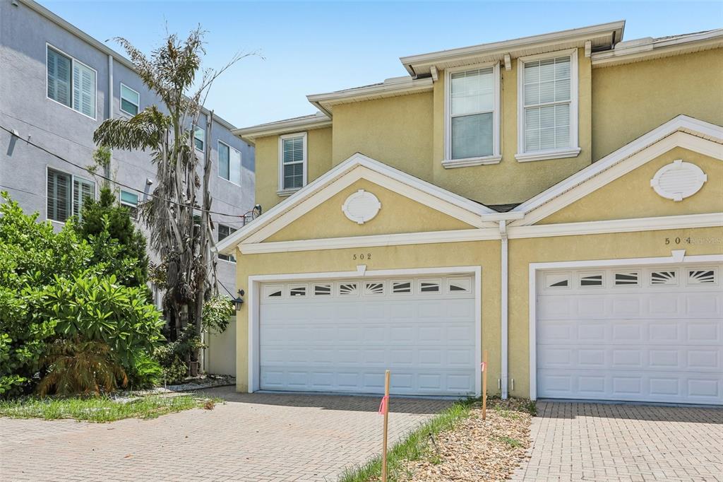 A yellow two-story townhouse with white garage doors and a brick paver driveway — 502 S LINCOLN AVENUE, TAMPA, FL