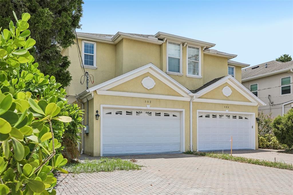 A two-story duplex with yellow stucco siding and two white garage doors sits on a driveway — 502 S LINCOLN AVENUE, TAMPA, FL