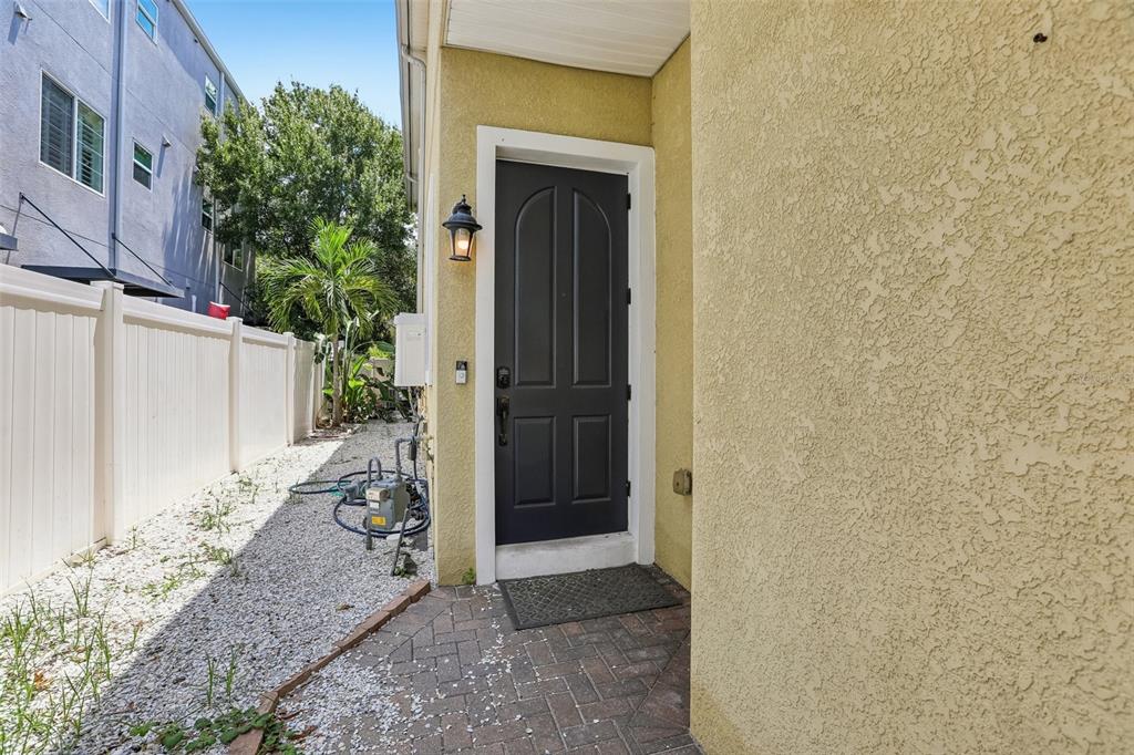 A dark front door is set into a yellow stucco wall beside a gravel walkway — 502 S LINCOLN AVENUE, TAMPA, FL