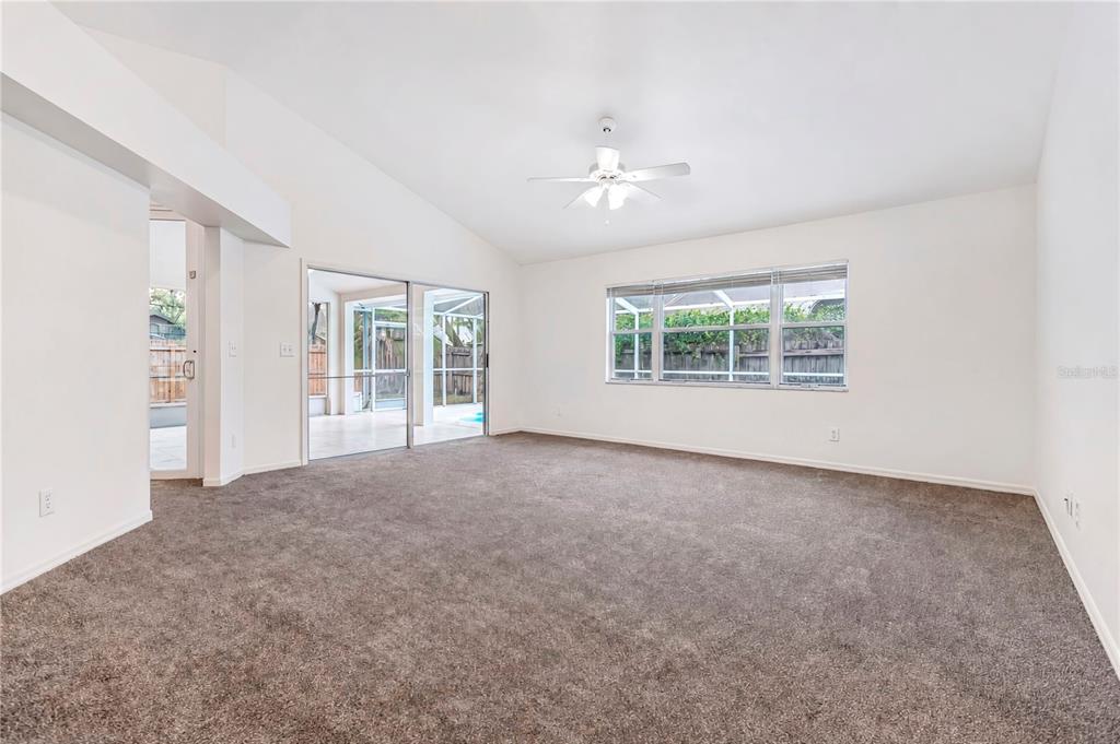 An empty living room features beige carpet, white walls, a ceiling fan, and sliding glass doors — 2302 LYNCREST COURT, VALRICO, FL