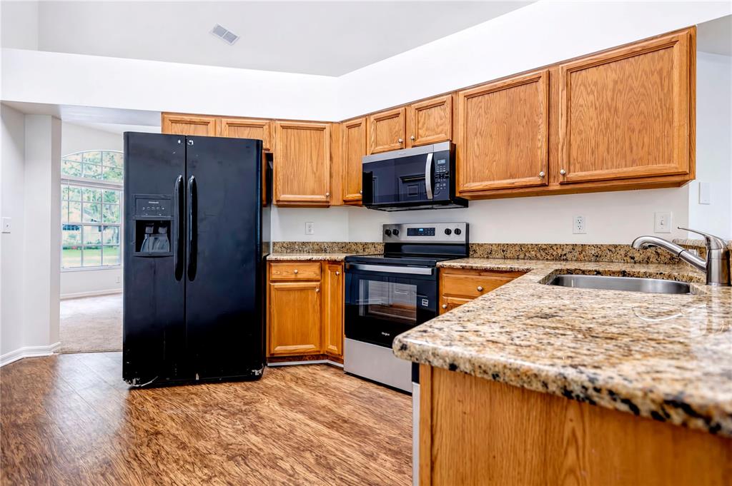 A kitchen features wood cabinets, granite countertops, a black refrigerator, and stainless steel appliances — 2302 LYNCREST COURT, VALRICO, FL
