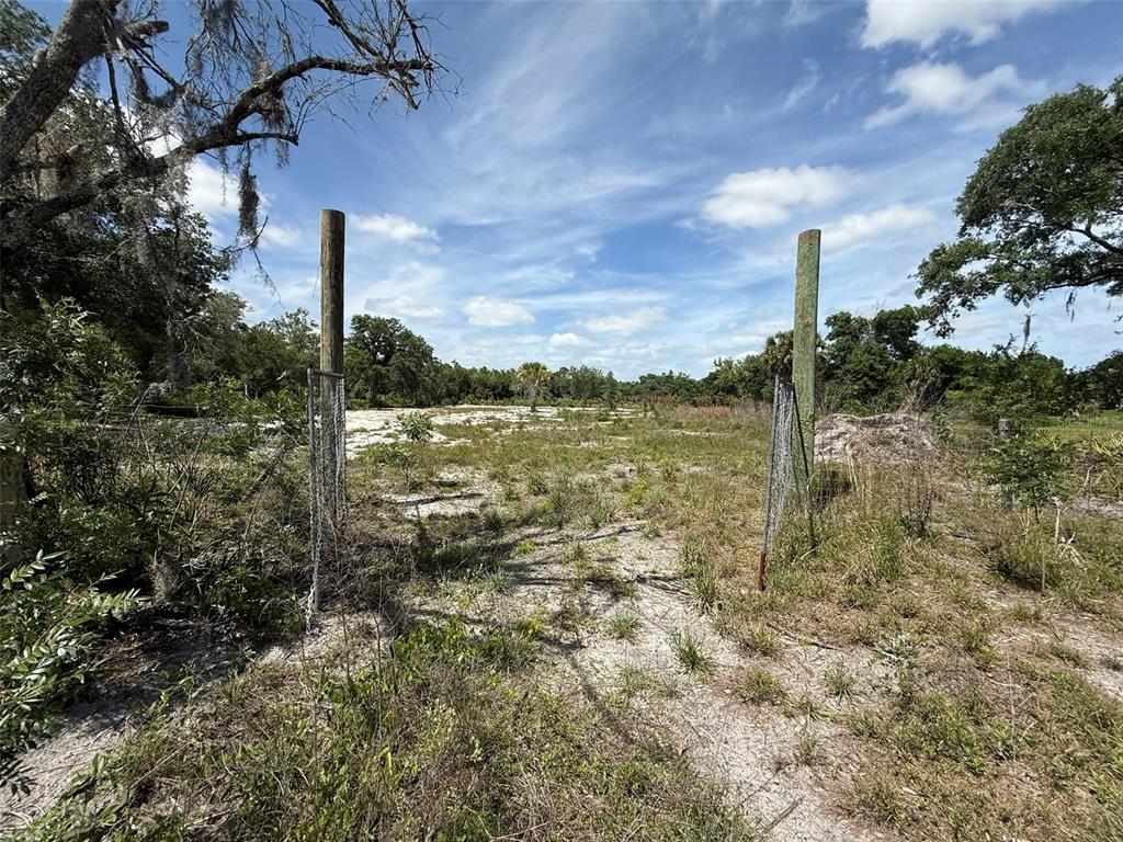 A dirt path leads through two wooden fence posts into a cleared, grassy lot — 18121 NW 256TH STREET, OKEECHOBEE, FL