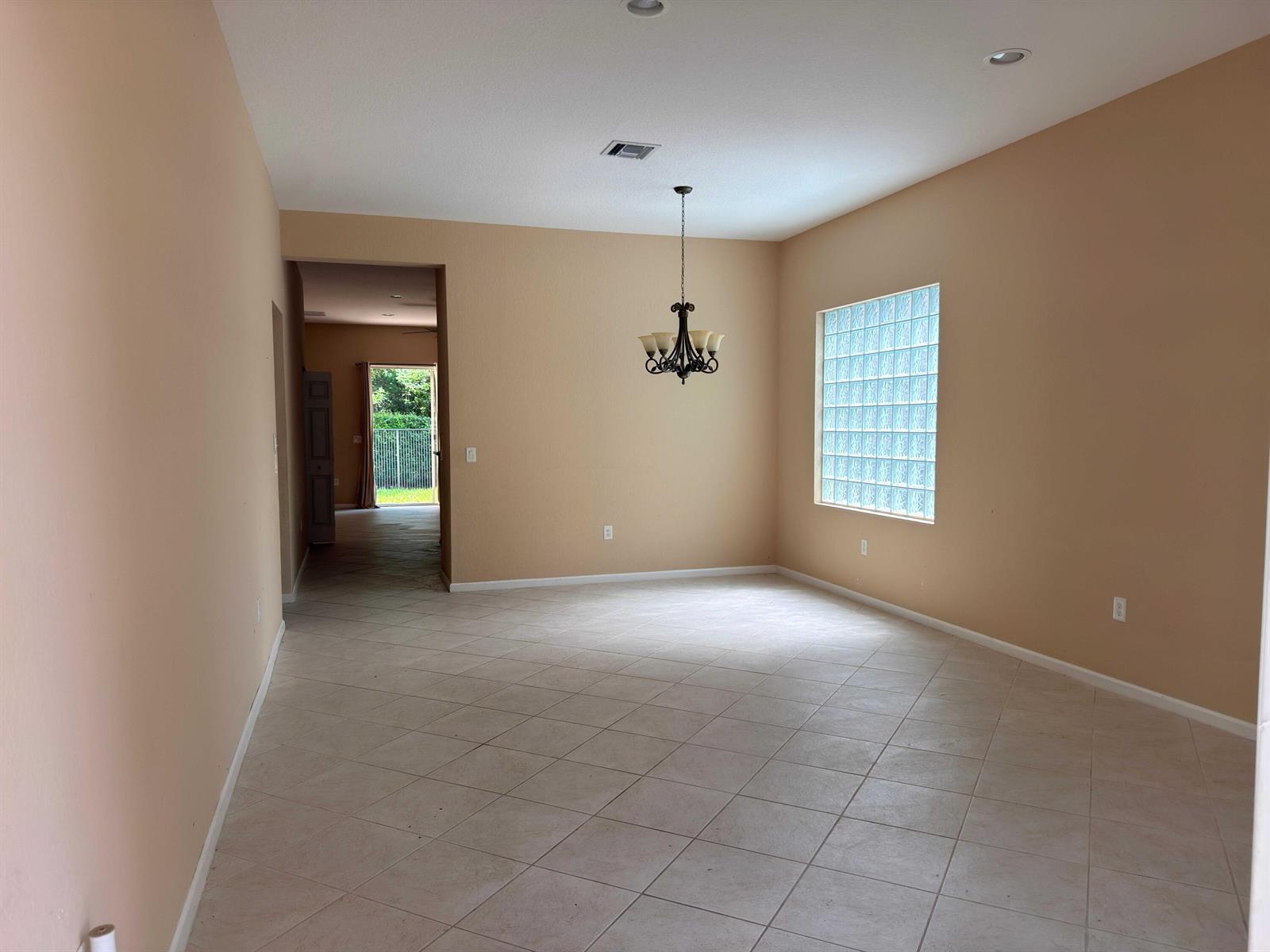 An empty dining room with tan walls, tile flooring, a chandelier, and a glass block window — 10172 White Water Lily Way, Boynton Beach FL 33437, BOYNTON BEACH, FL