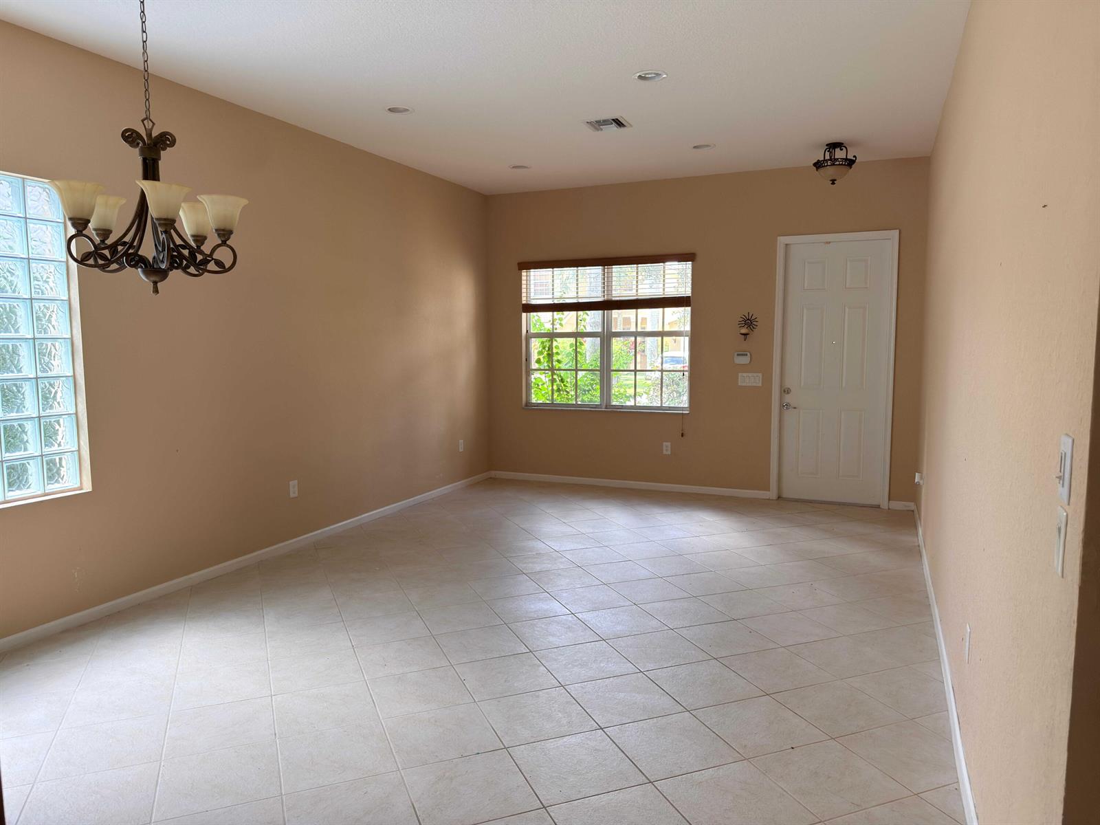 An empty room features beige walls, tile flooring, a chandelier, and a glass block window — 10172 White Water Lily Way, Boynton Beach FL 33437, BOYNTON BEACH, FL
