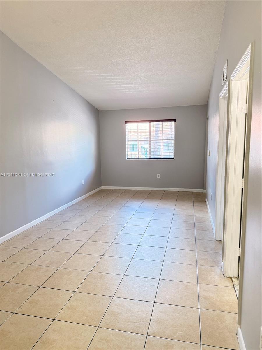 This empty room features gray walls, beige tile flooring, and a single window — 2930 SE 12th Rd # 31, Homestead FL 33035, HOMESTEAD, FL