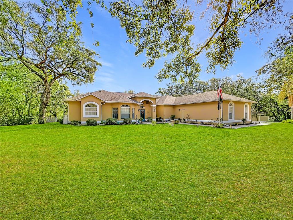 A single-story tan house with a large green lawn and mature trees — 10301 FOX SPARROW AVENUE, WEEKI WACHEE, FL