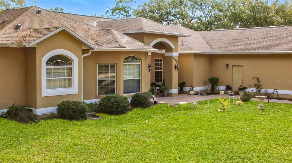 A tan single-story house with a brown shingled roof and a grassy front yard — 10301 FOX SPARROW AVENUE, WEEKI WACHEE, FL