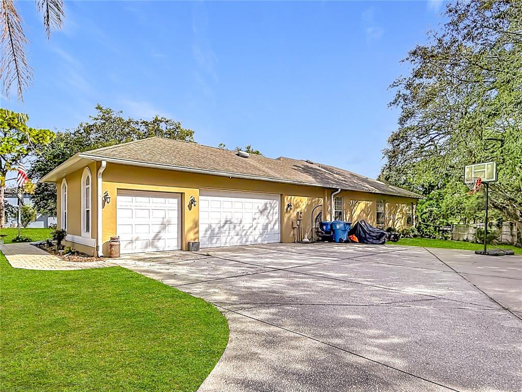 A yellow house with a three-car garage and a large concrete driveway — 10301 FOX SPARROW AVENUE, WEEKI WACHEE, FL